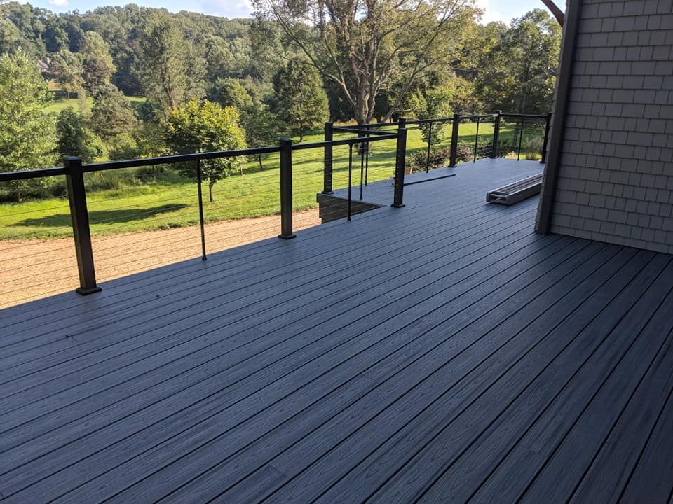 A gray deck with a black railing and a view of a field.