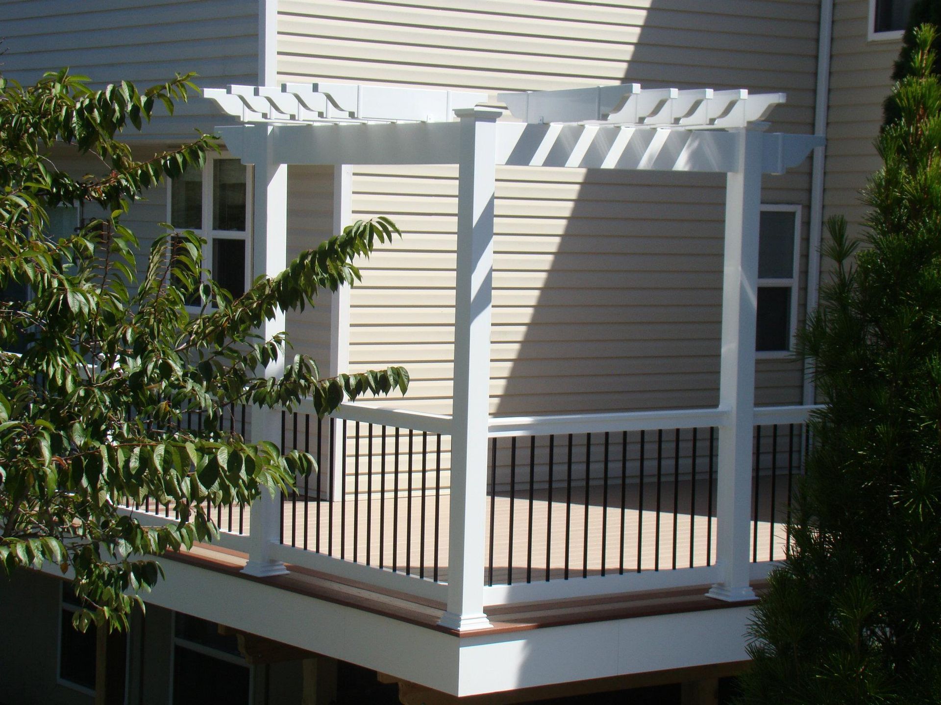 A white pergola sits on a deck in front of a house