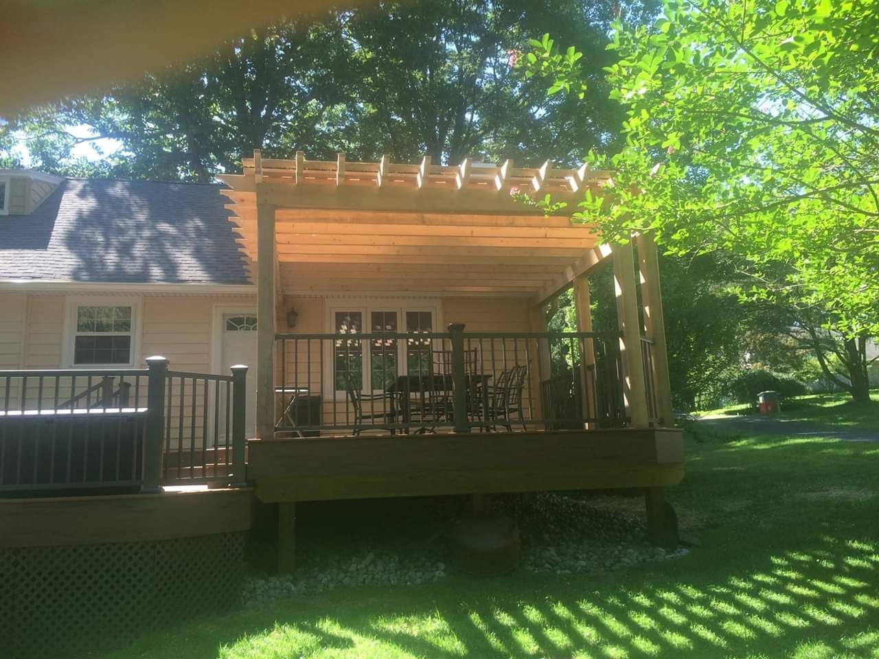 A wooden deck with a pergola over it is in the backyard of a house.