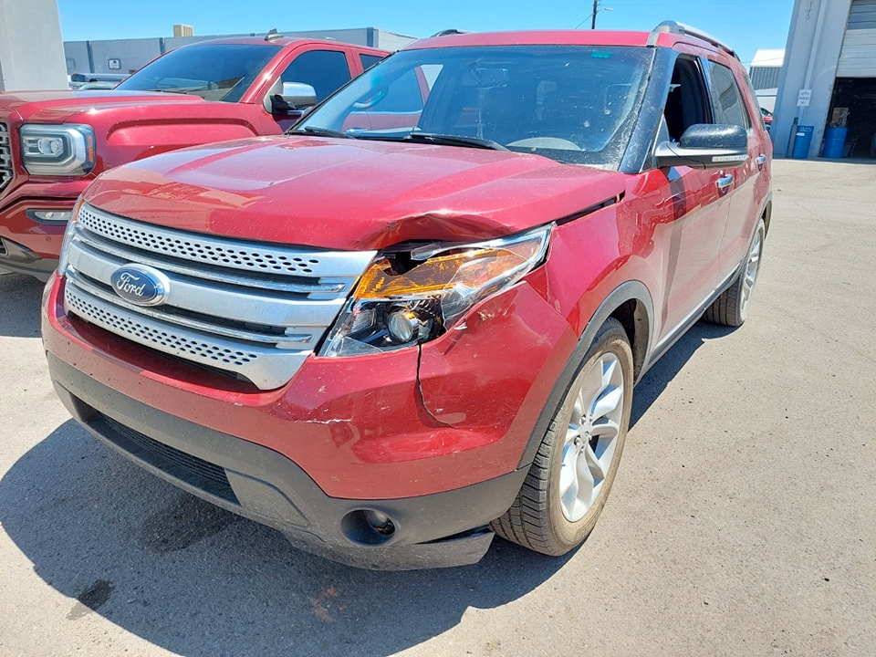 A red ford explorer with a damaged headlight is parked in a parking lot.