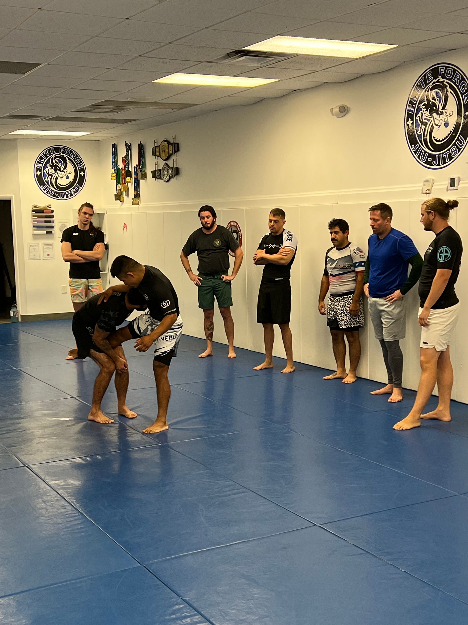 A group of men are standing around a blue mat in a gym.