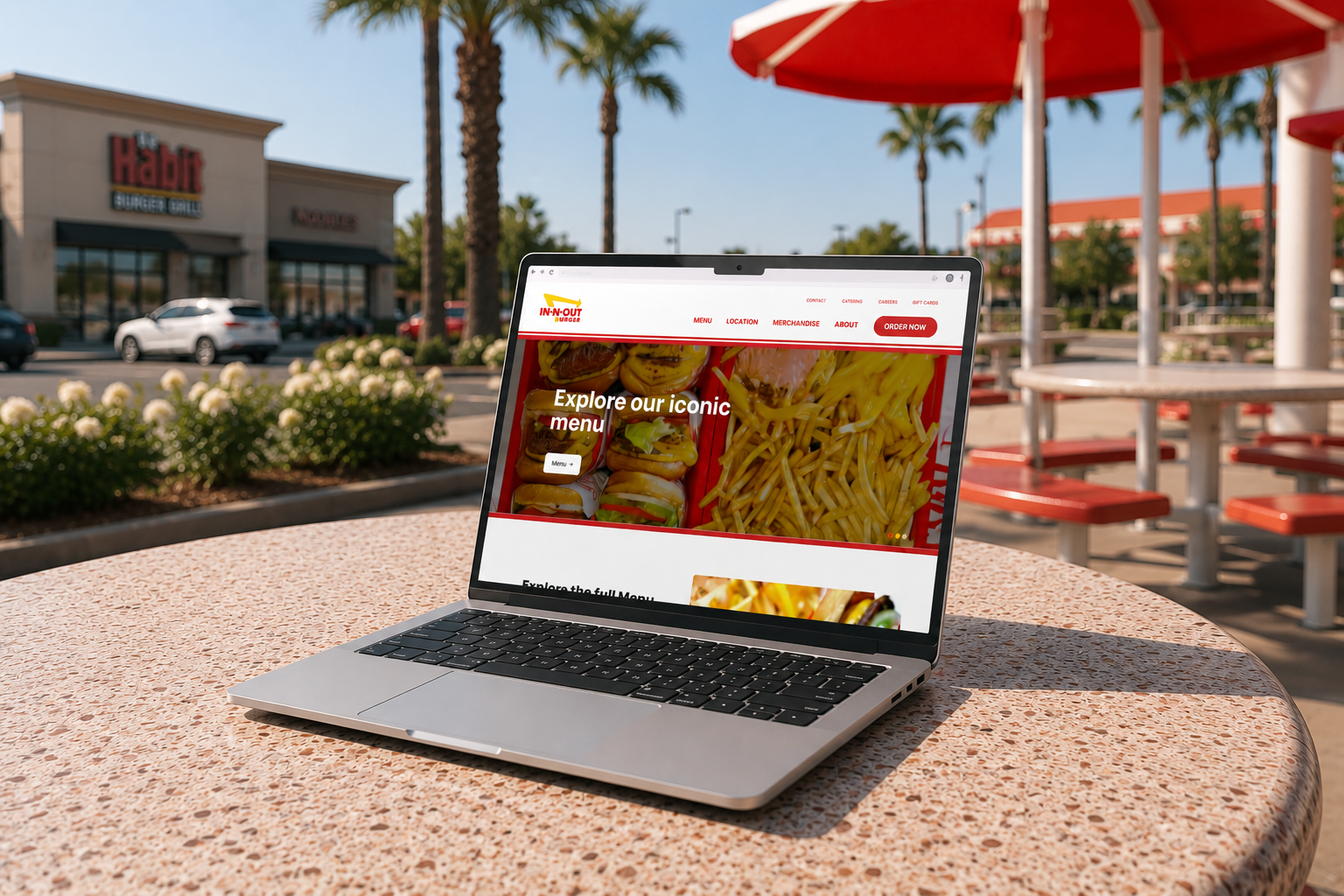 Laptop on a patio table displaying a restaurant website with red umbrellas and storefront in the background