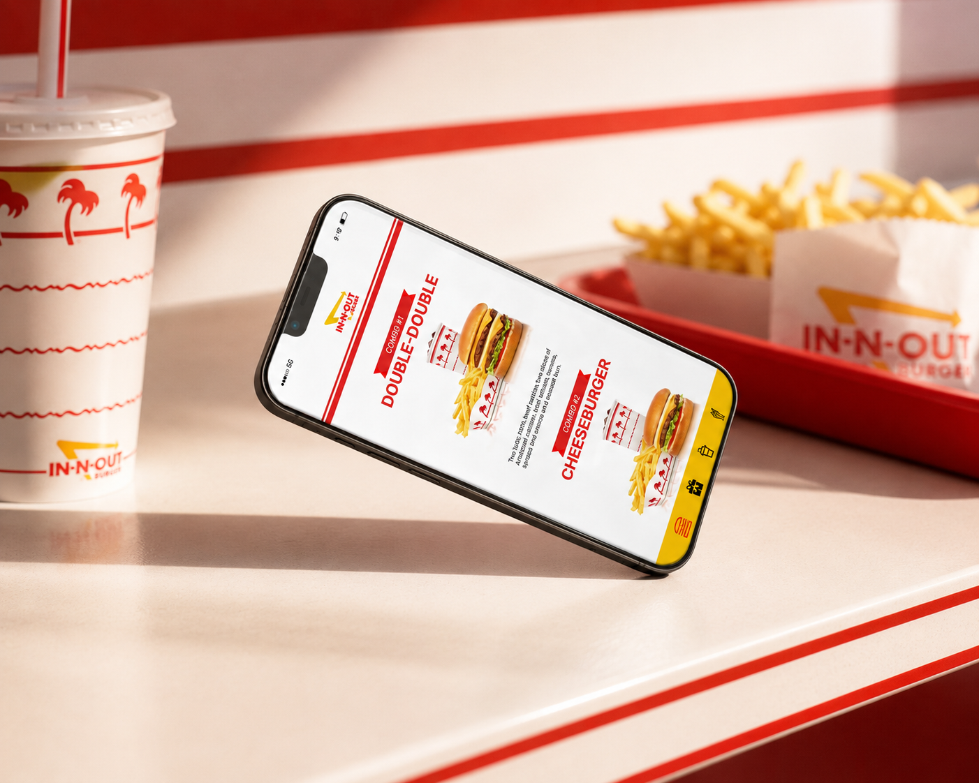 Smartphone displaying In-N-Out menu, propped on a tray table beside a drink and fries