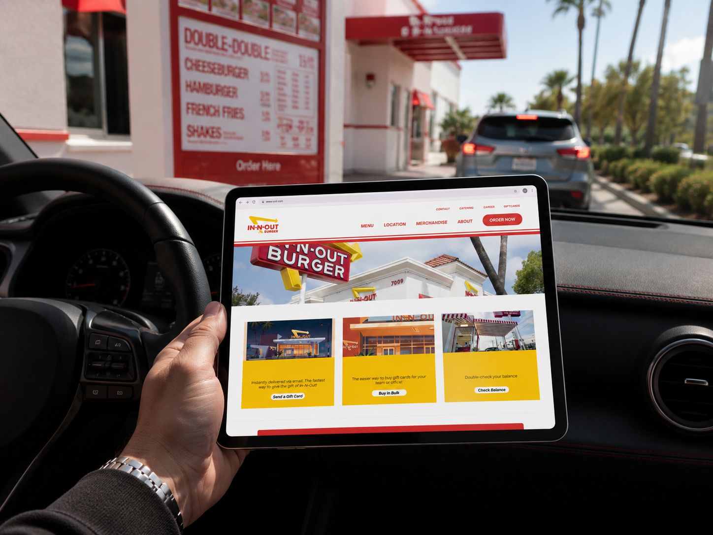 Person holding tablet displaying a restaurant website in a drive-thru lane