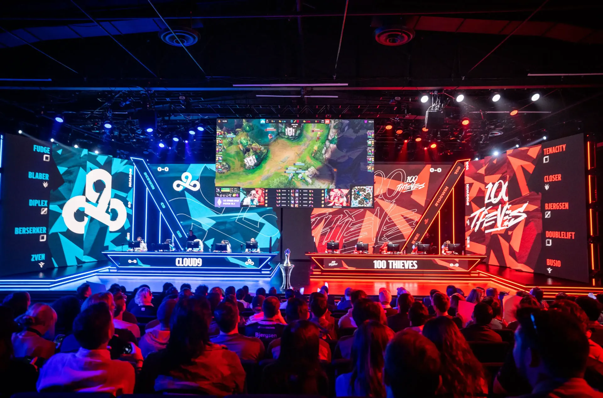 Esports tournament stage with two teams facing off in blue and red-lit gaming booths before a crowd