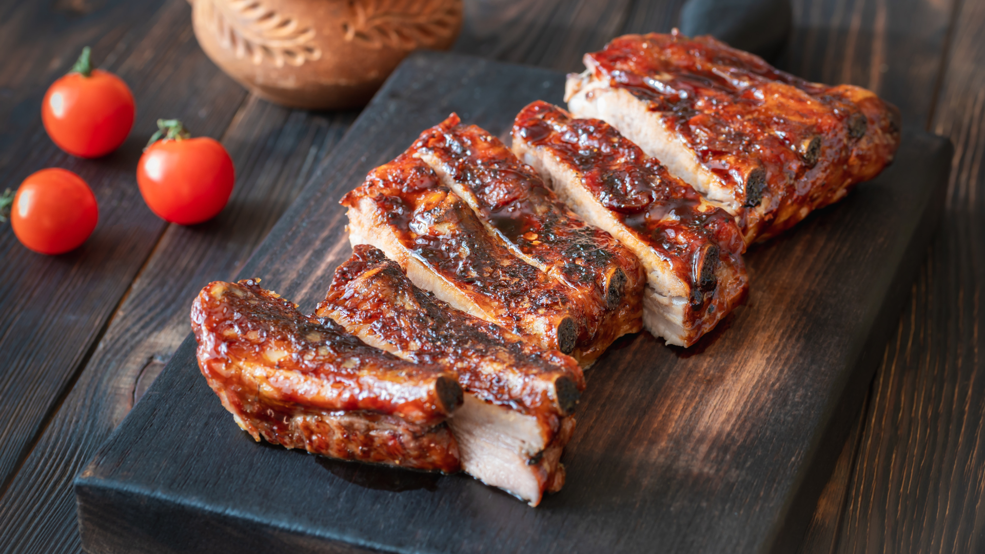 A cutting board topped with ribs and tomatoes on a wooden table.