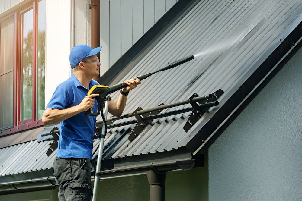 A Man Is Cleaning The Roof Of A House — Alta Cleaning Service In Palmerston, NT