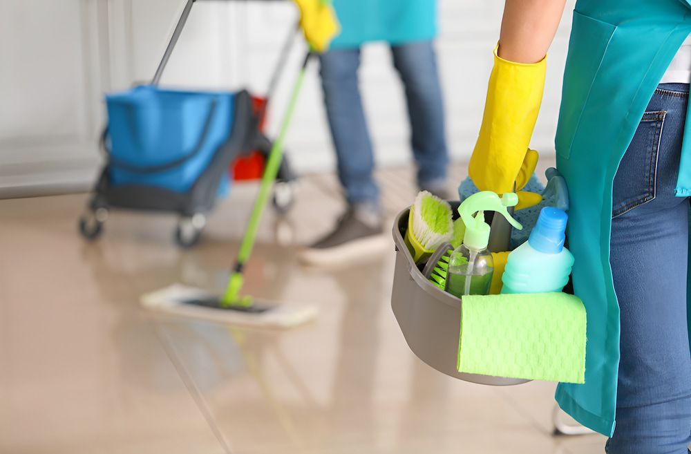 A Woman Is Holding A Bucket Of Cleaning Supplies — Alta Cleaning Service In Darwin, NT