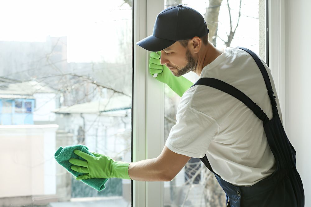 A Person Wearing Green Gloves Is Cleaning A Window — Alta Cleaning Service In Palmerston, NT