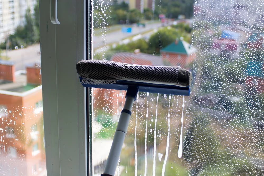 A Person Is Cleaning A Window With A Squeegee — Alta Cleaning Service In Palmerston, NT
