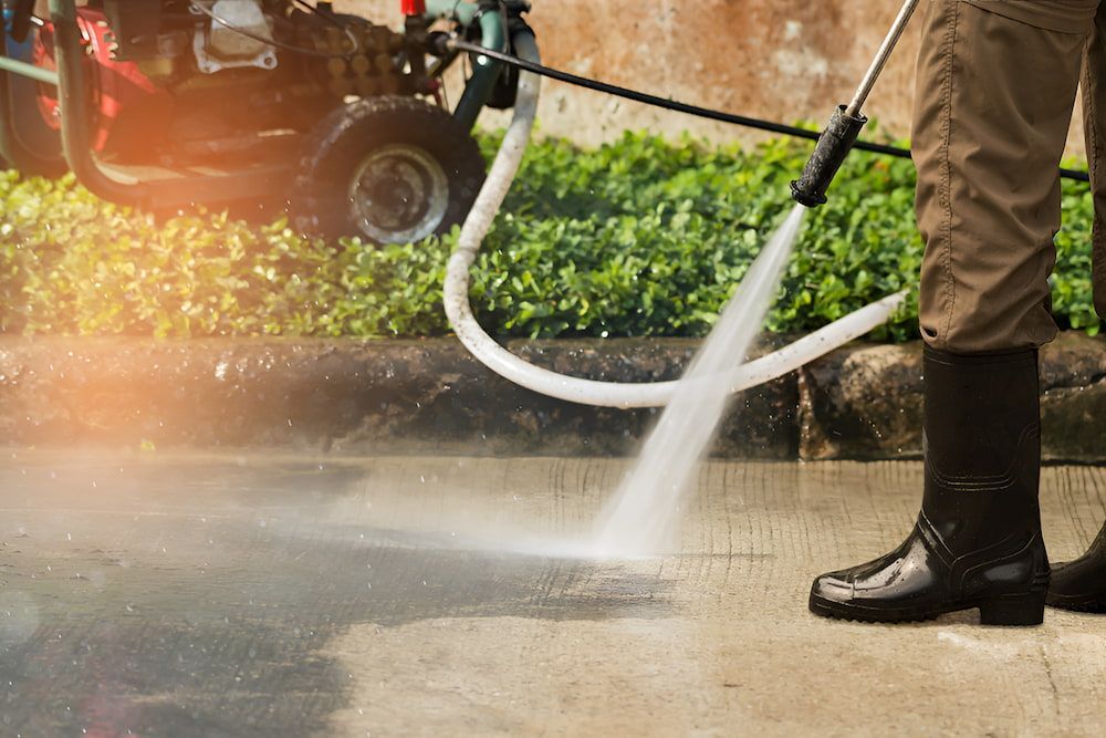 A Man Is Using A High Pressure Washer To Clean A Sidewalk — Alta Cleaning Service In Palmerston, NT