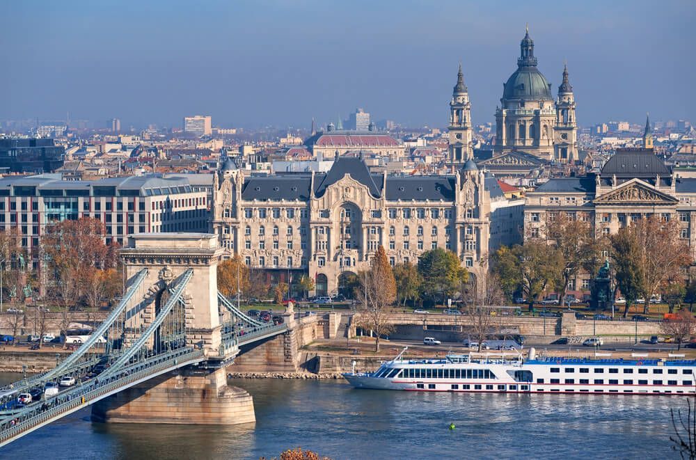 A Boat Is Going Under A Bridge Over A River In Front Of A City — Métier Medical Ltd in Hamburg, Germany