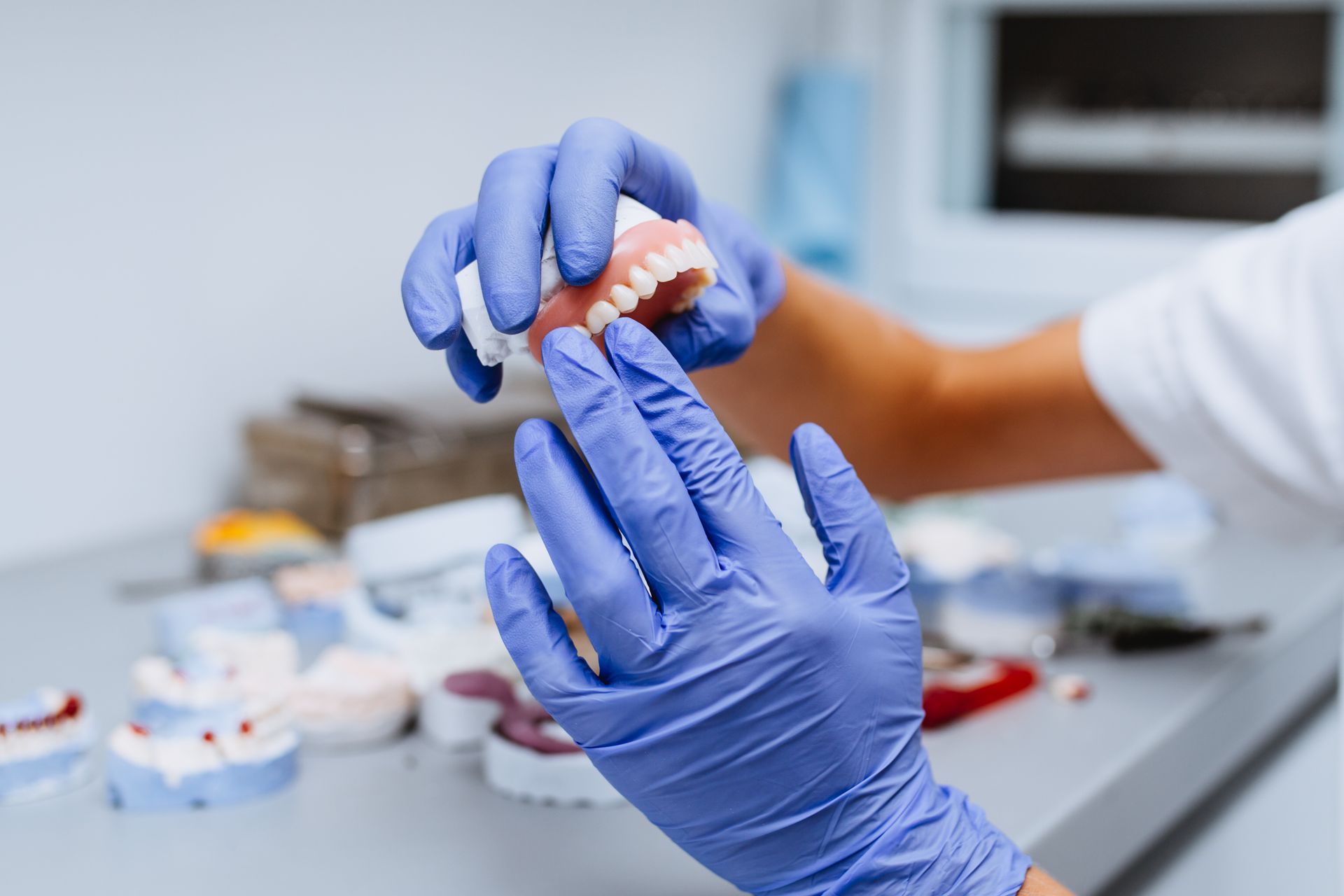 Hands in blue gloves holding and examining dentures in a dental office setting.