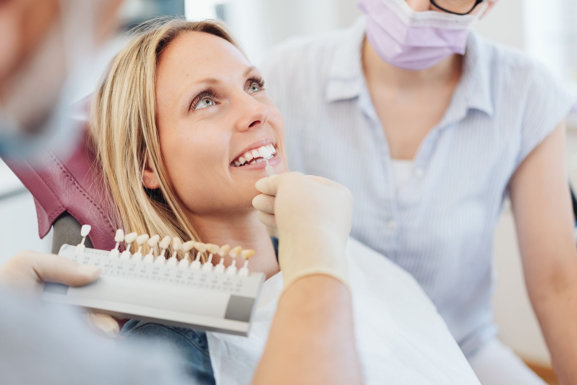 Woman having teeth shade matched by a dentist. A dental assistant stands by her side.