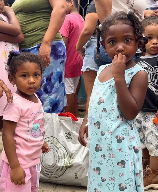 Two little girls are standing next to each other in front of a group of people.