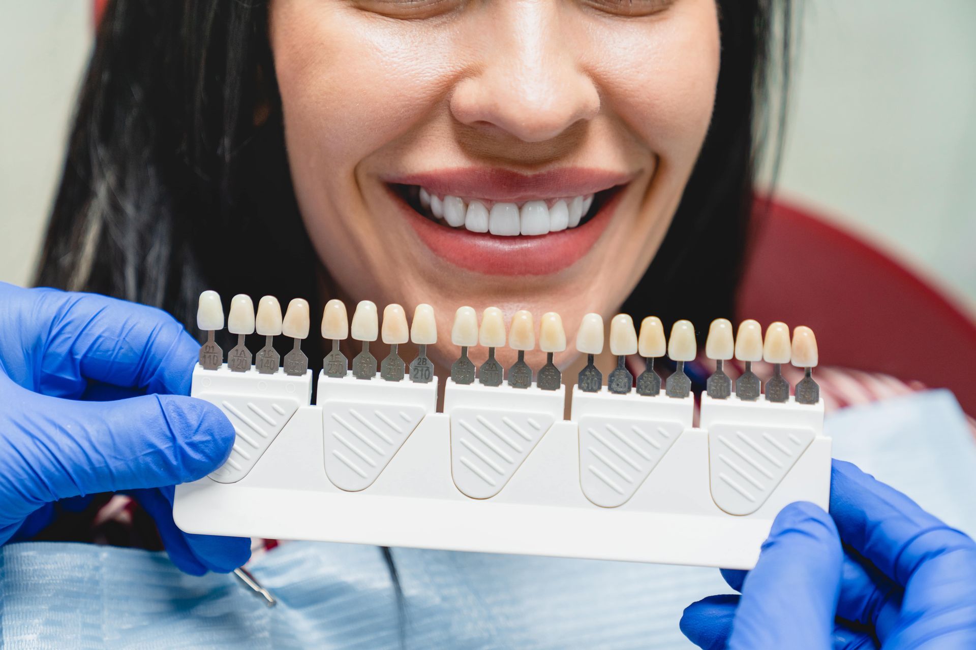 Dentist holding a shade guide next to a patient's bright, white teeth in a dental office.