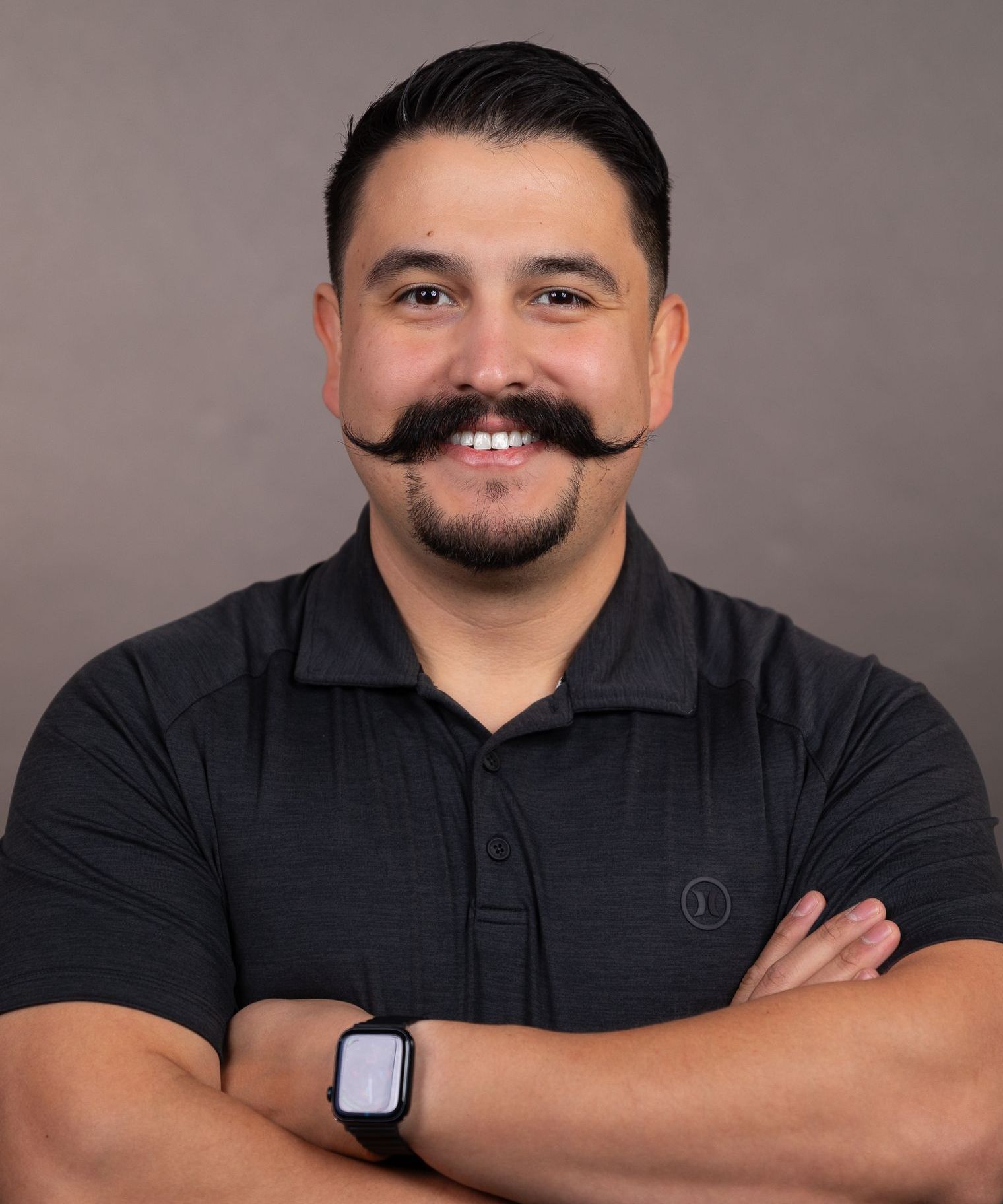 A man with a mustache is wearing a black shirt and a watch.