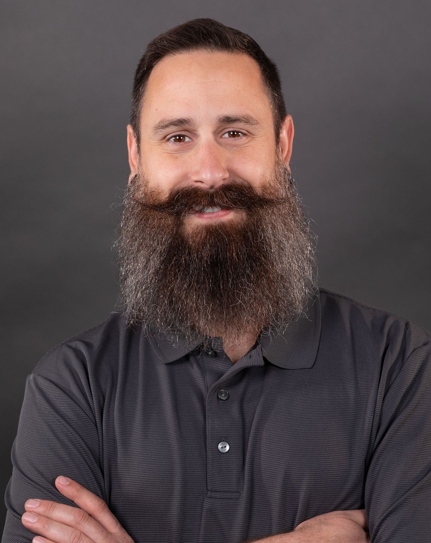 A man with a beard and mustache is standing with his arms crossed.