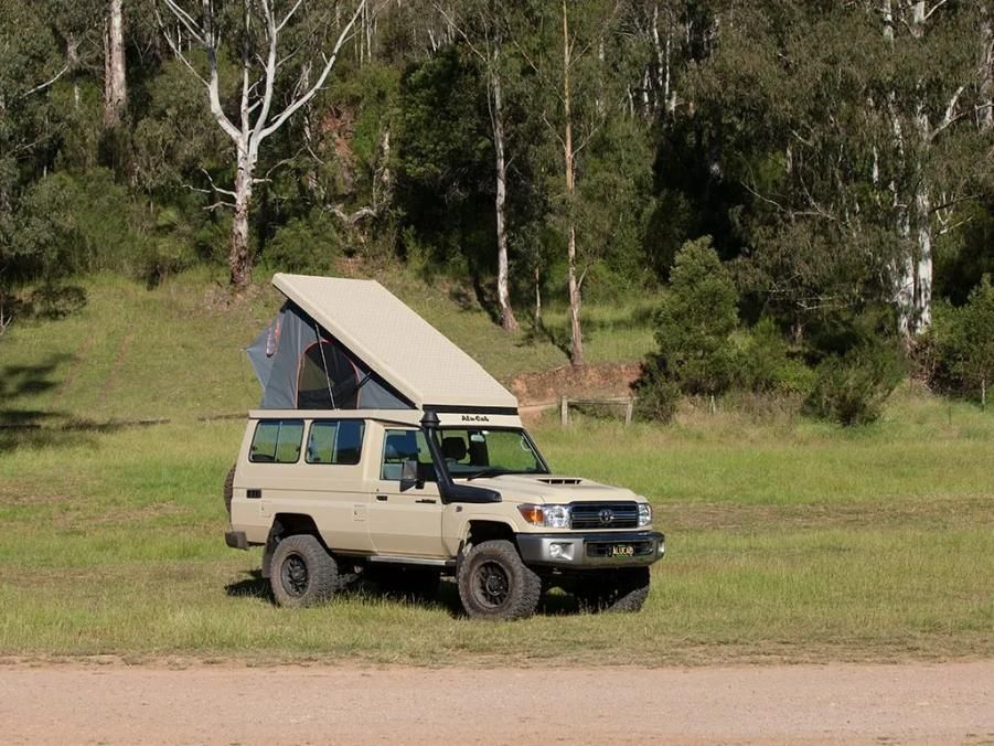 A Truck With a Tent on Top of It is Parked in a Grassy Field — Whitsunday 4x4 & Automotive In Cannonvale, QLD
