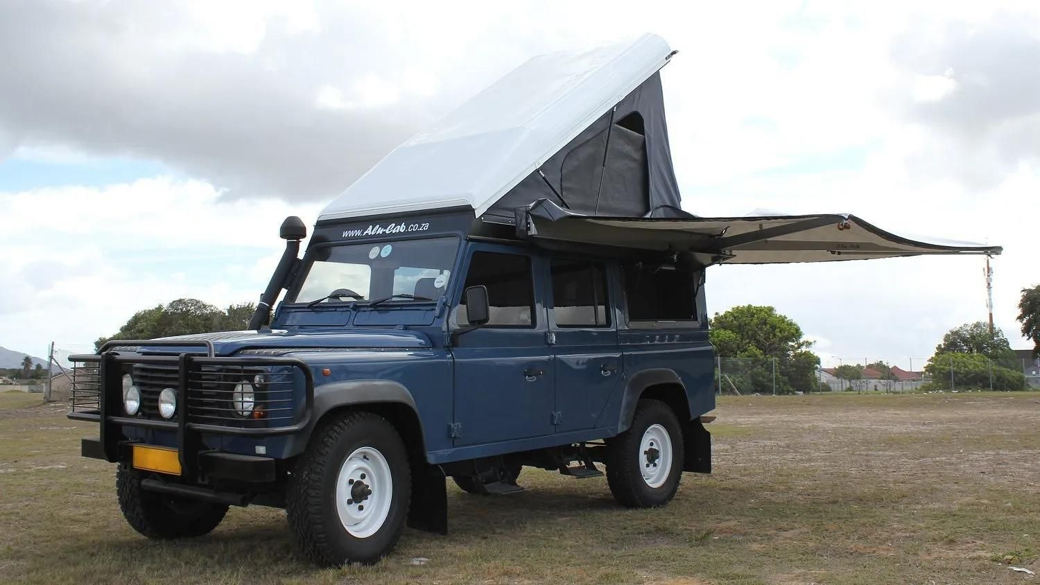 A Blue Land Rover With a Tent on Top of It is Parked in a Field — Whitsunday 4x4 & Automotive In Cannonvale, QLD