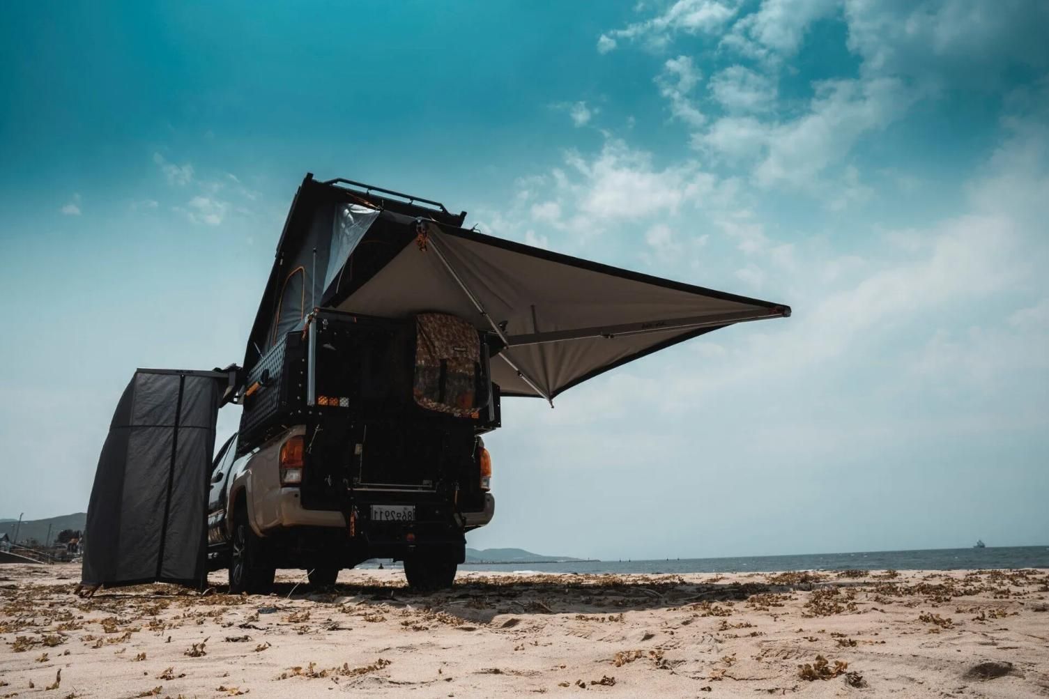 A Truck With a Tent on Top of It is Parked on the Beach — Whitsunday 4x4 & Automotive In Cannonvale, QLD