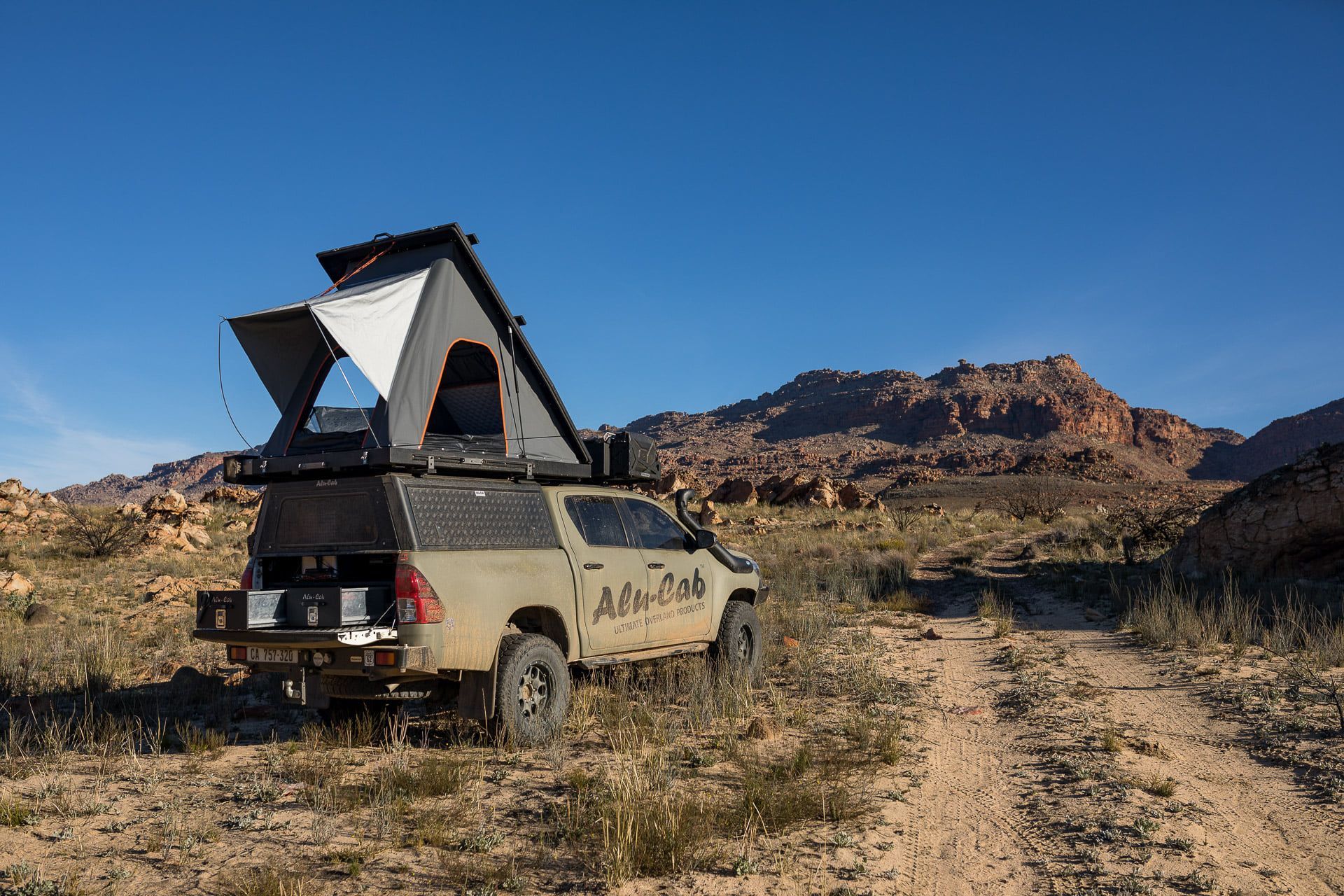 Desert camper van with rooftop tent parked on a rocky dirt track beside mountains under a clear blue sky — Whitsunday 4x4 & Automotive In Proserpine, QLD