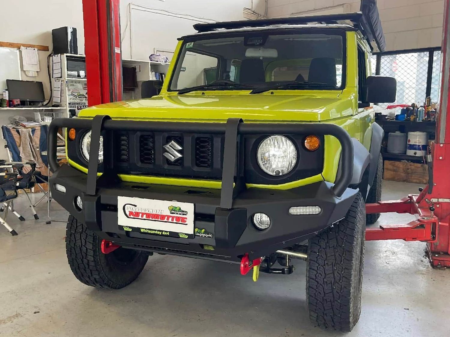 A Yellow Suzuki Jimny is Parked on a Lift in a Garage — Whitsunday 4x4 & Automotive In Airlie Beach, QLD