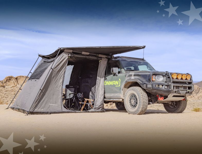 A truck is parked in the desert with a tent attached to it.