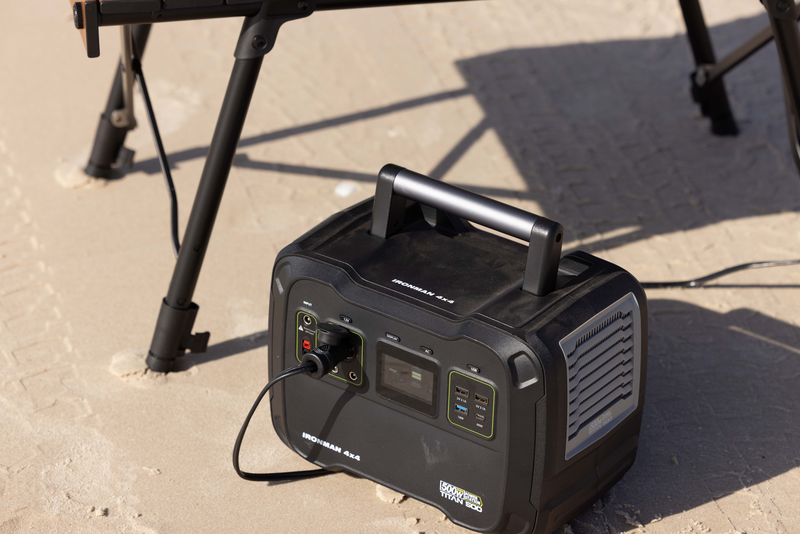 A black portable power station is sitting on the ground next to a chair.