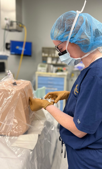 Medical professional performing a procedure on a training mannequin in a medical setting.