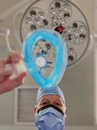 Surgeon in mask about to administer anesthesia with a blue mask, surgical light in background.