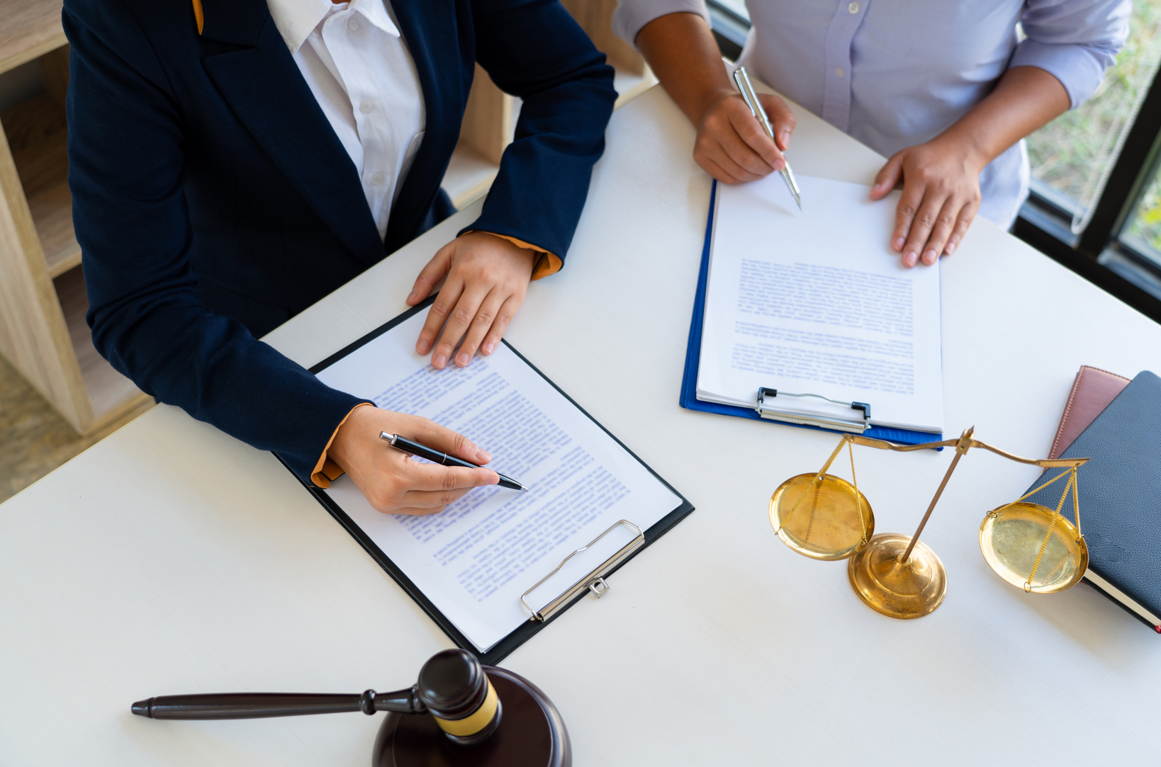 Two lawyers are sitting at a table with a gavel and scales of justice.