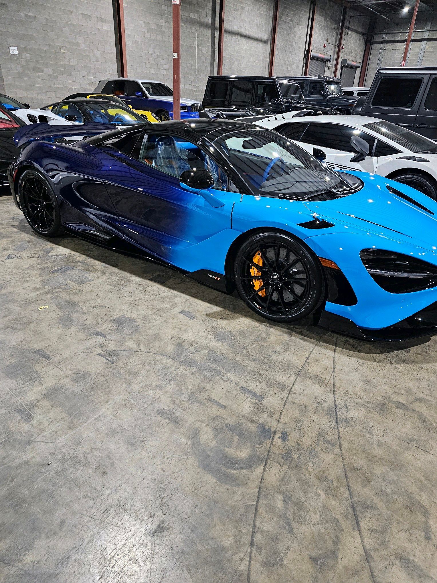 Blue and black McLaren sports car parked inside a garage, with other vehicles in the background.