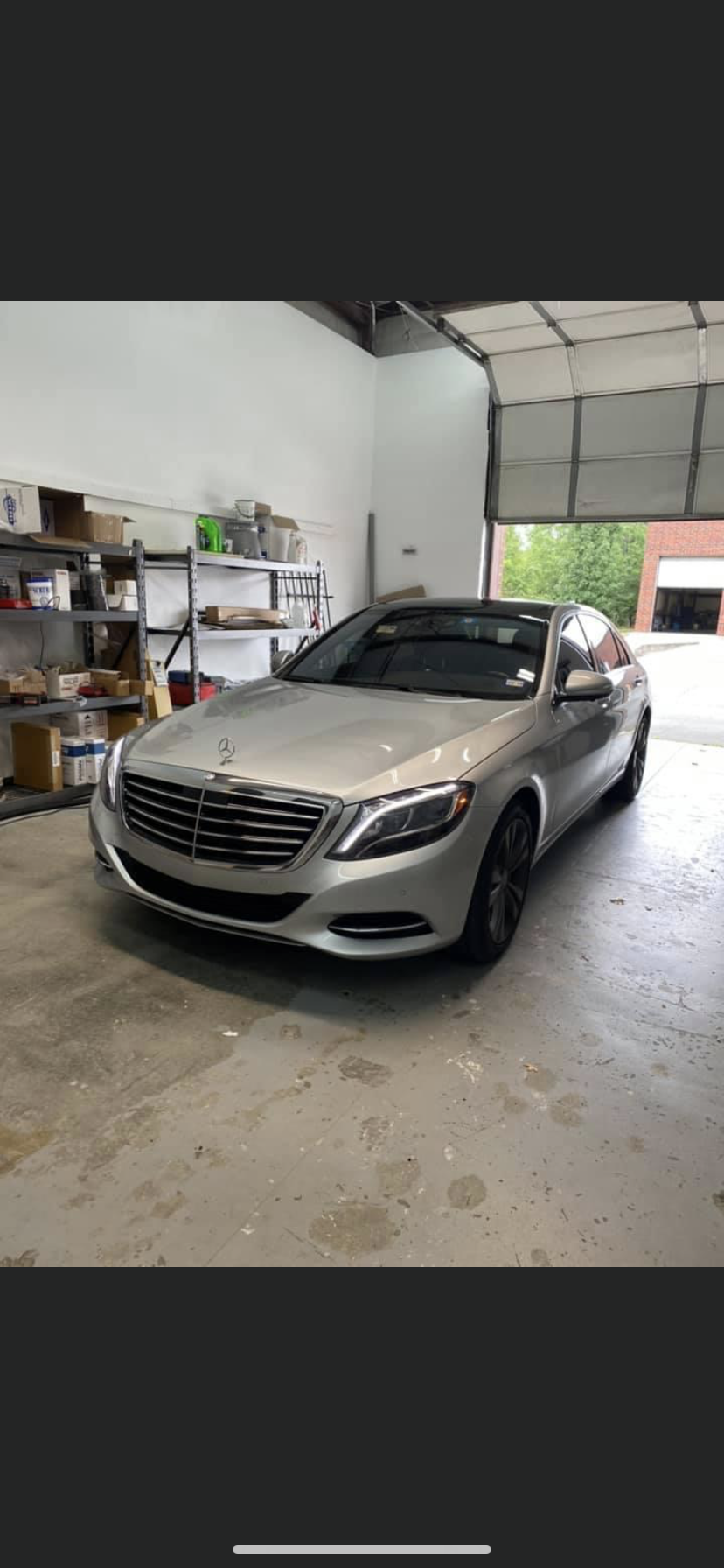 Silver Mercedes-Benz sedan parked inside a garage, with the open door revealing greenery.
