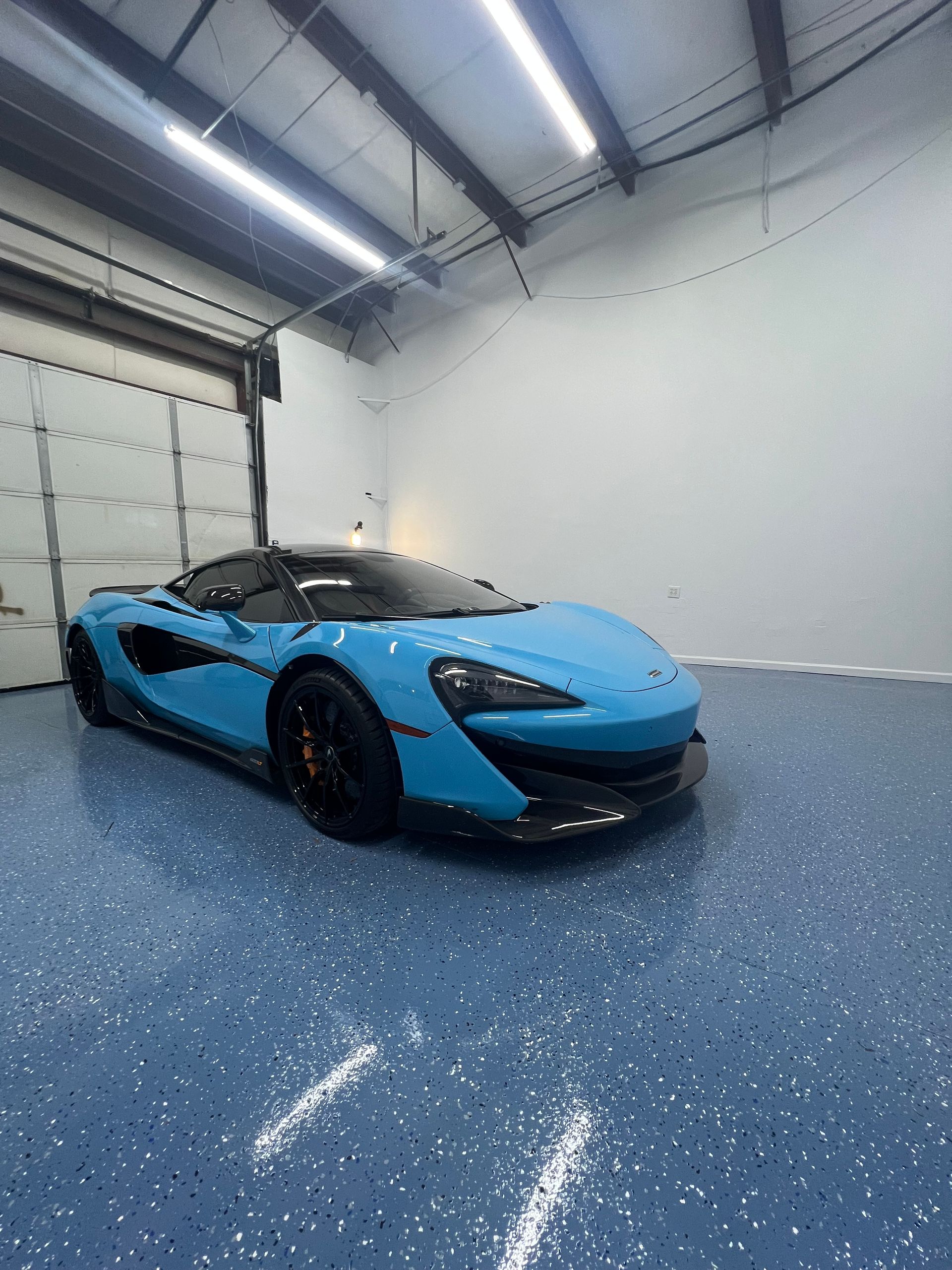 Blue McLaren sports car parked inside a garage with blue speckled floor.