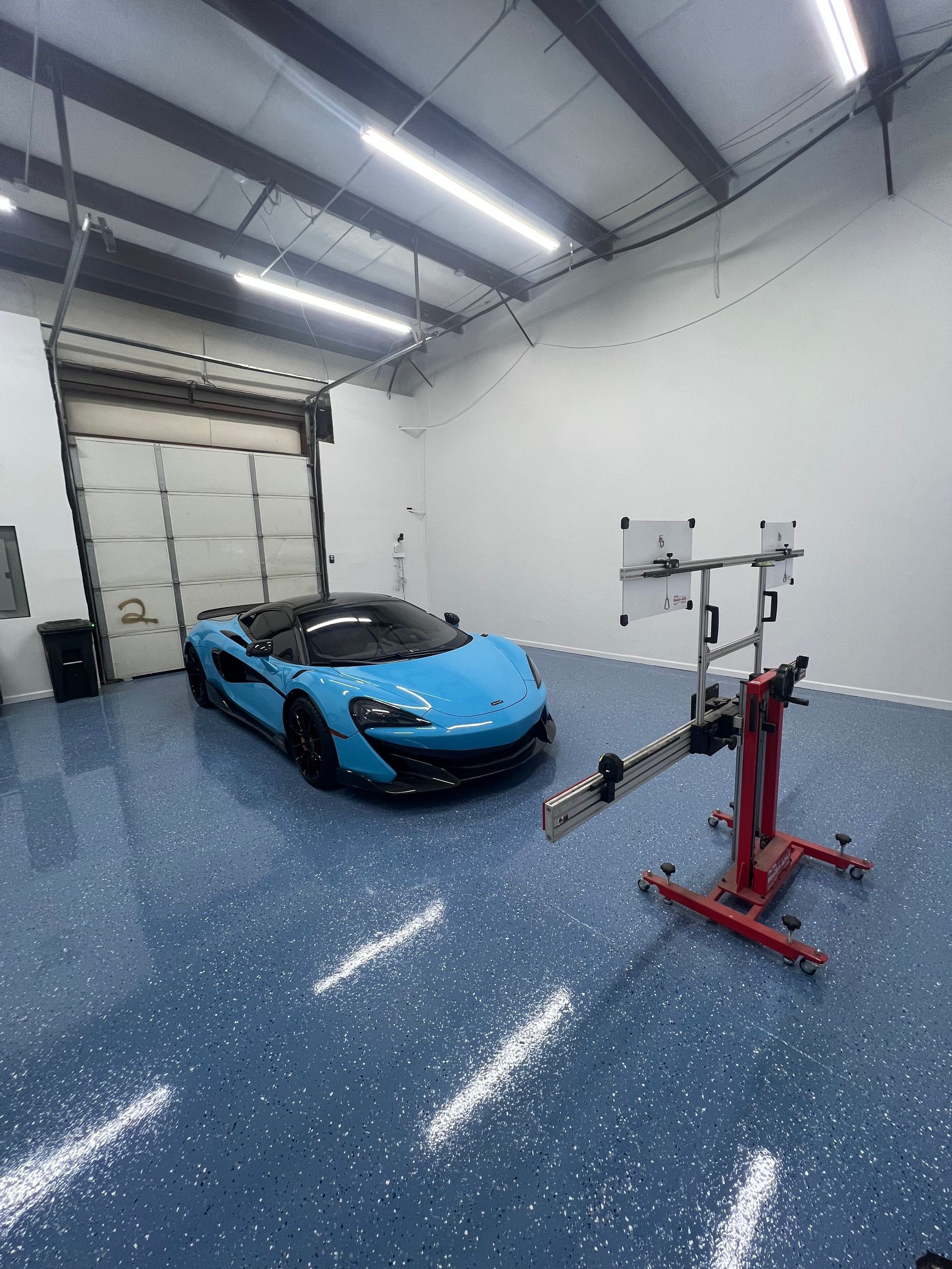 Light blue McLaren sports car in a garage with a wheel alignment machine.