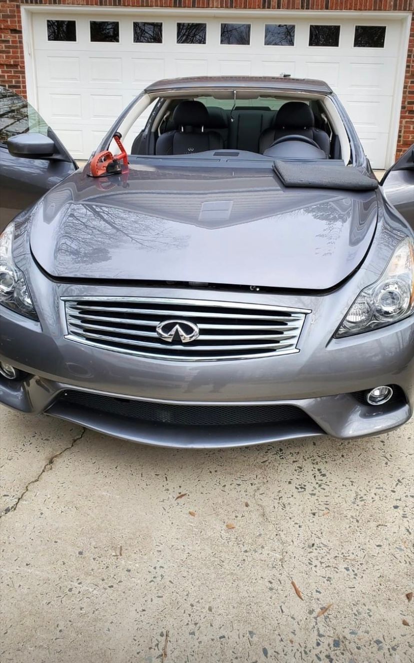 Gray Infiniti car with the hood open, parked in front of a white garage door.