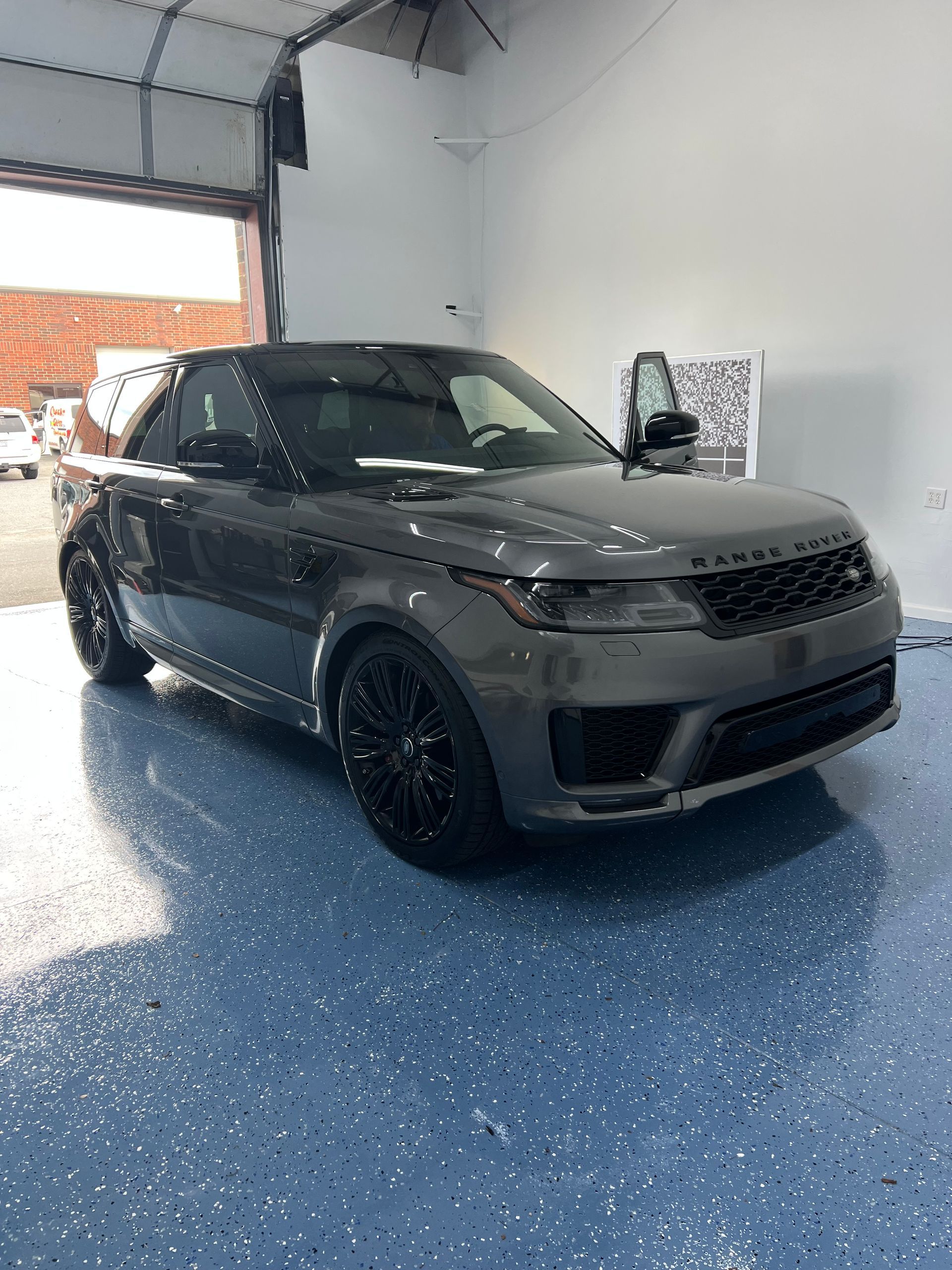 Gray Range Rover Sport SUV parked inside a garage with epoxy flooring and an open bay door.