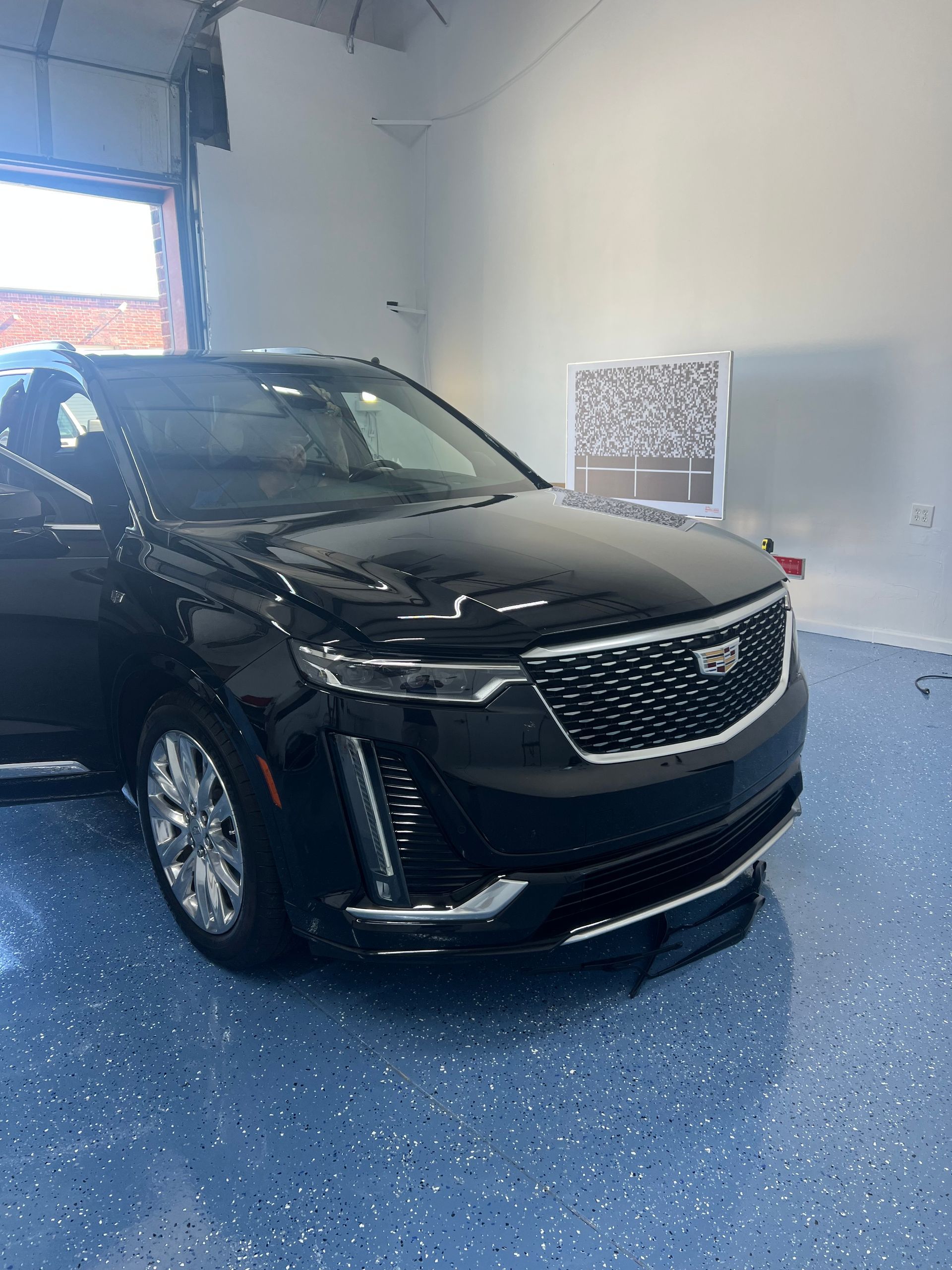 Black Cadillac SUV in a brightly lit indoor space with a blue floor.