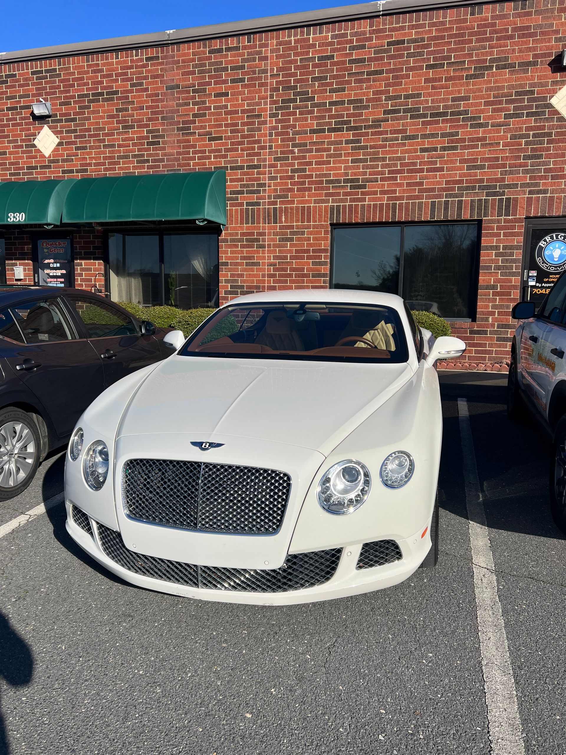 White Bentley parked in front of a brick building with a green awning.
