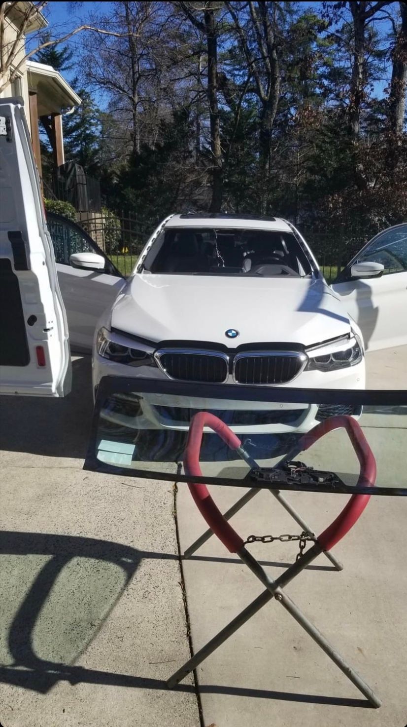 White BMW car being worked on outside, windshield replacement. Red stand, white van.