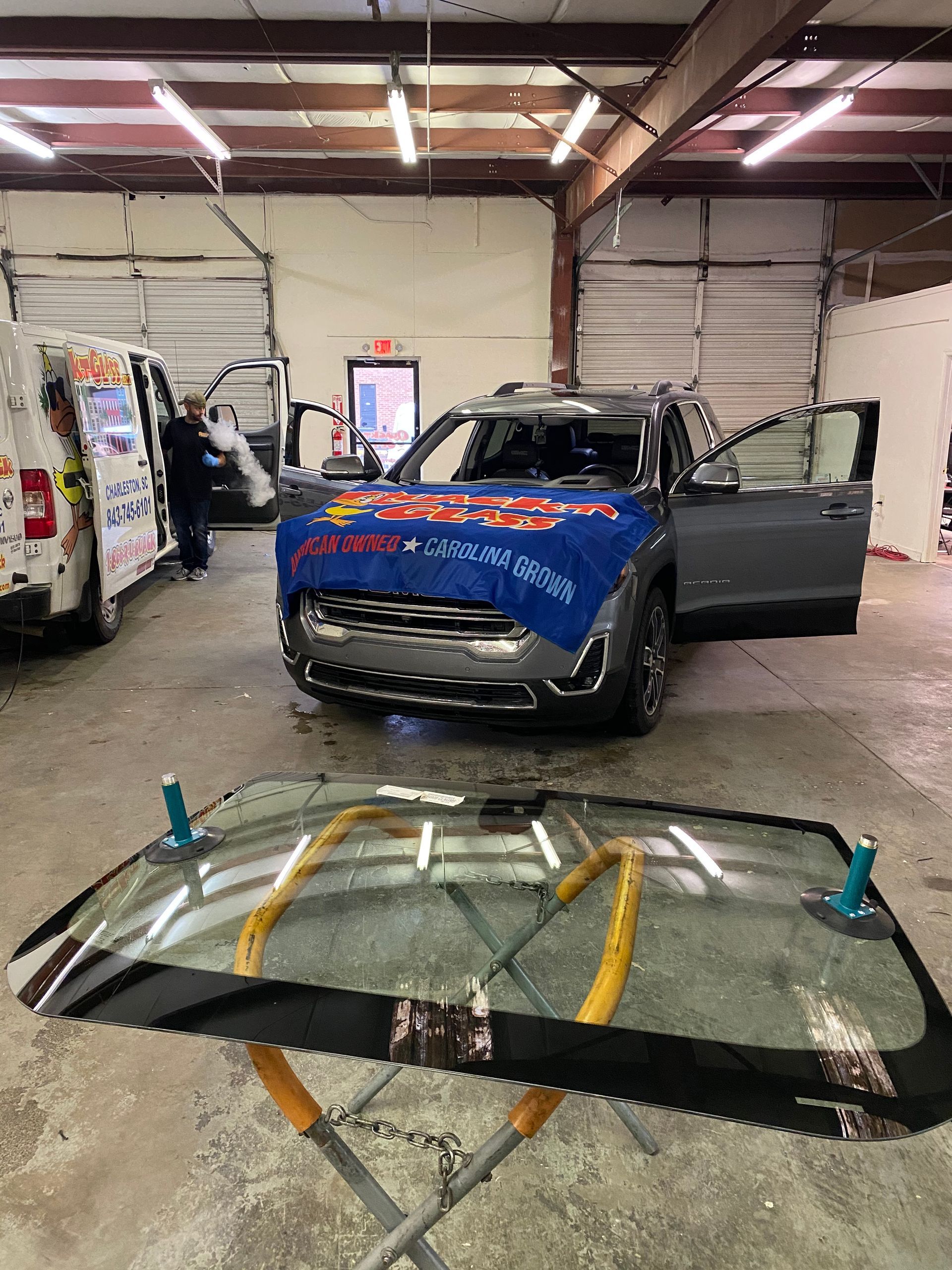 Windshield replacement in progress at a shop: car with new windshield, person working, tools.
