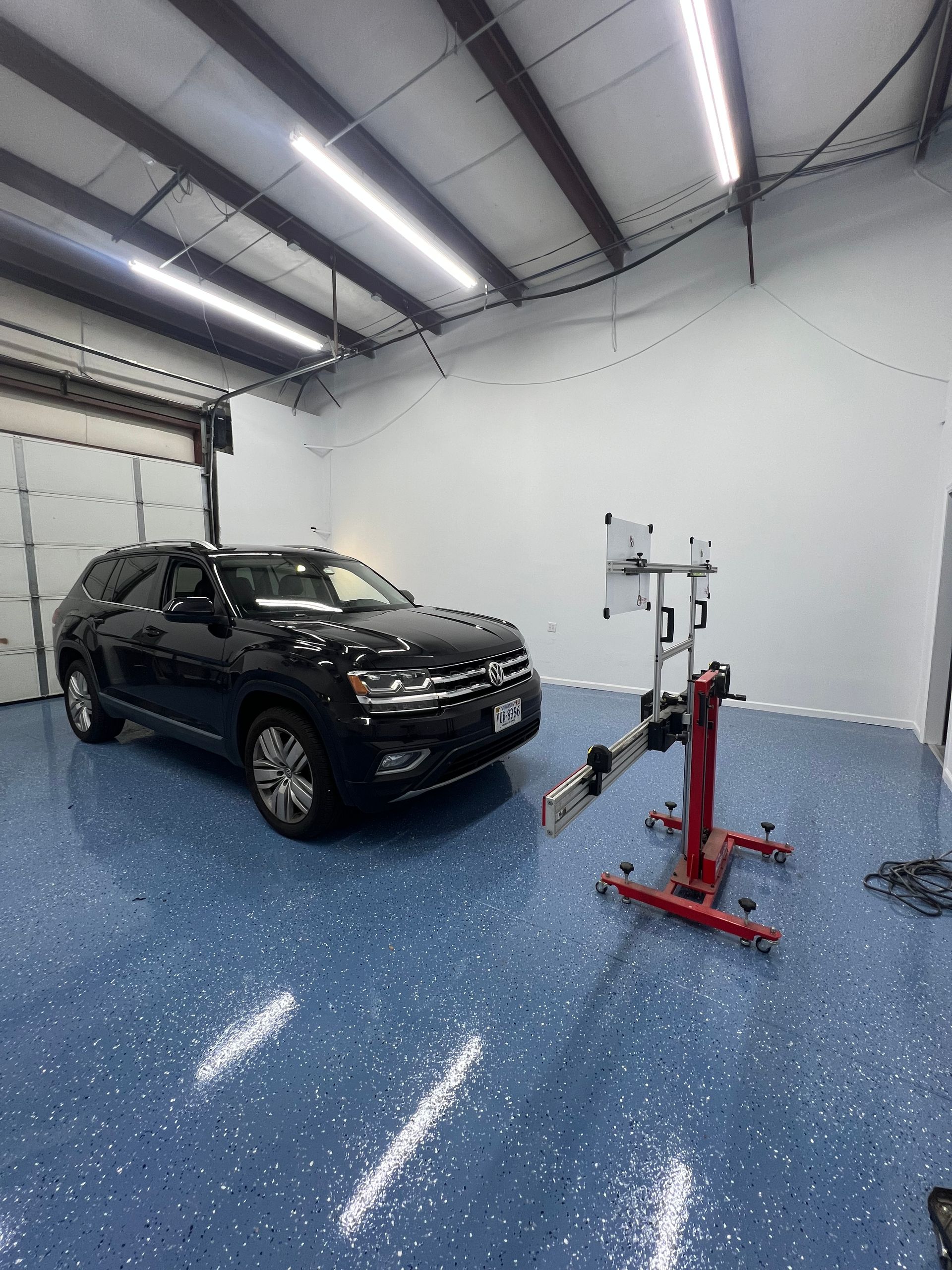 Black SUV in a garage being aligned by a machine on a blue speckled floor.