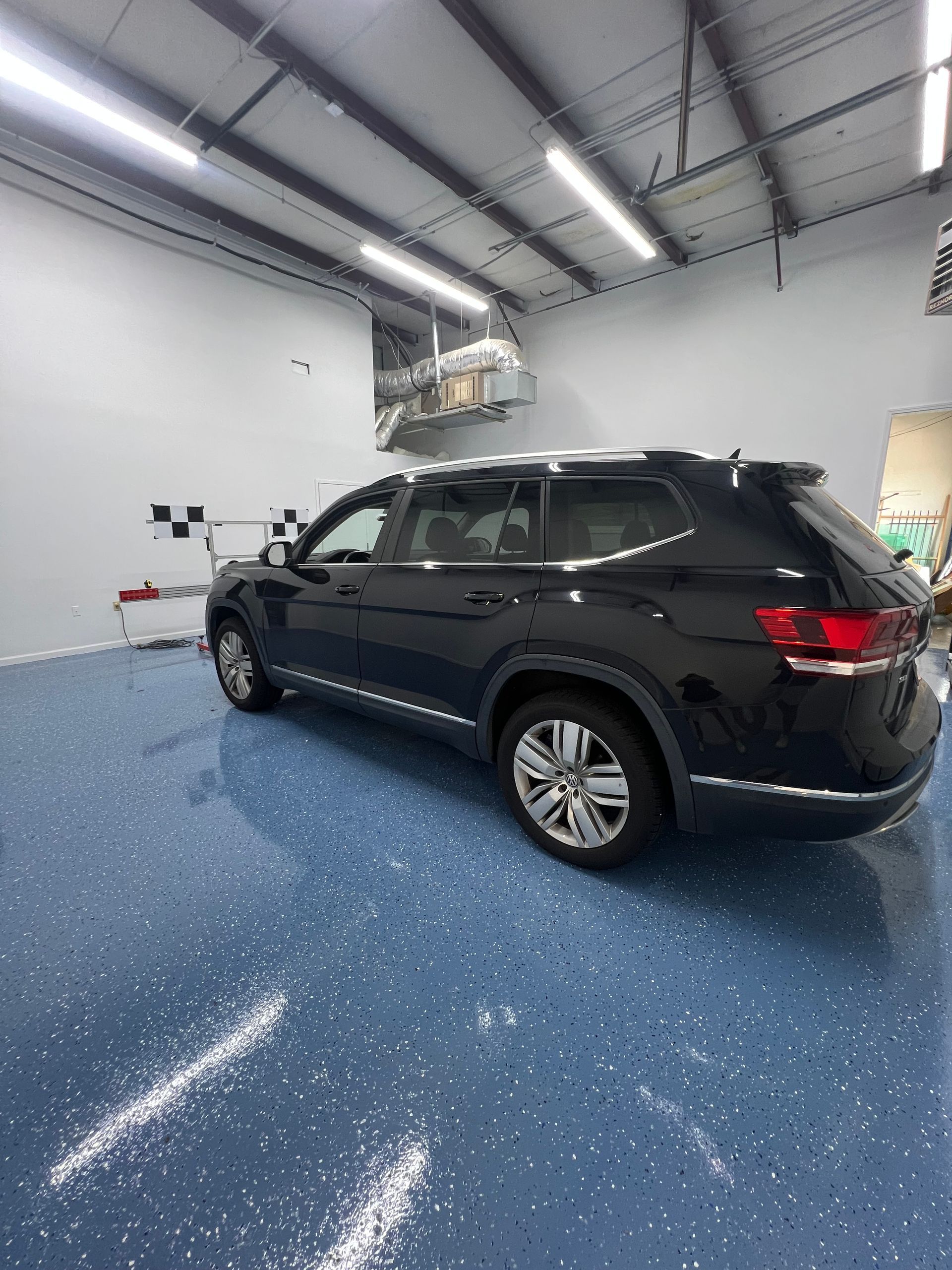 Black SUV parked inside a garage with blue epoxy floor, under fluorescent lights.