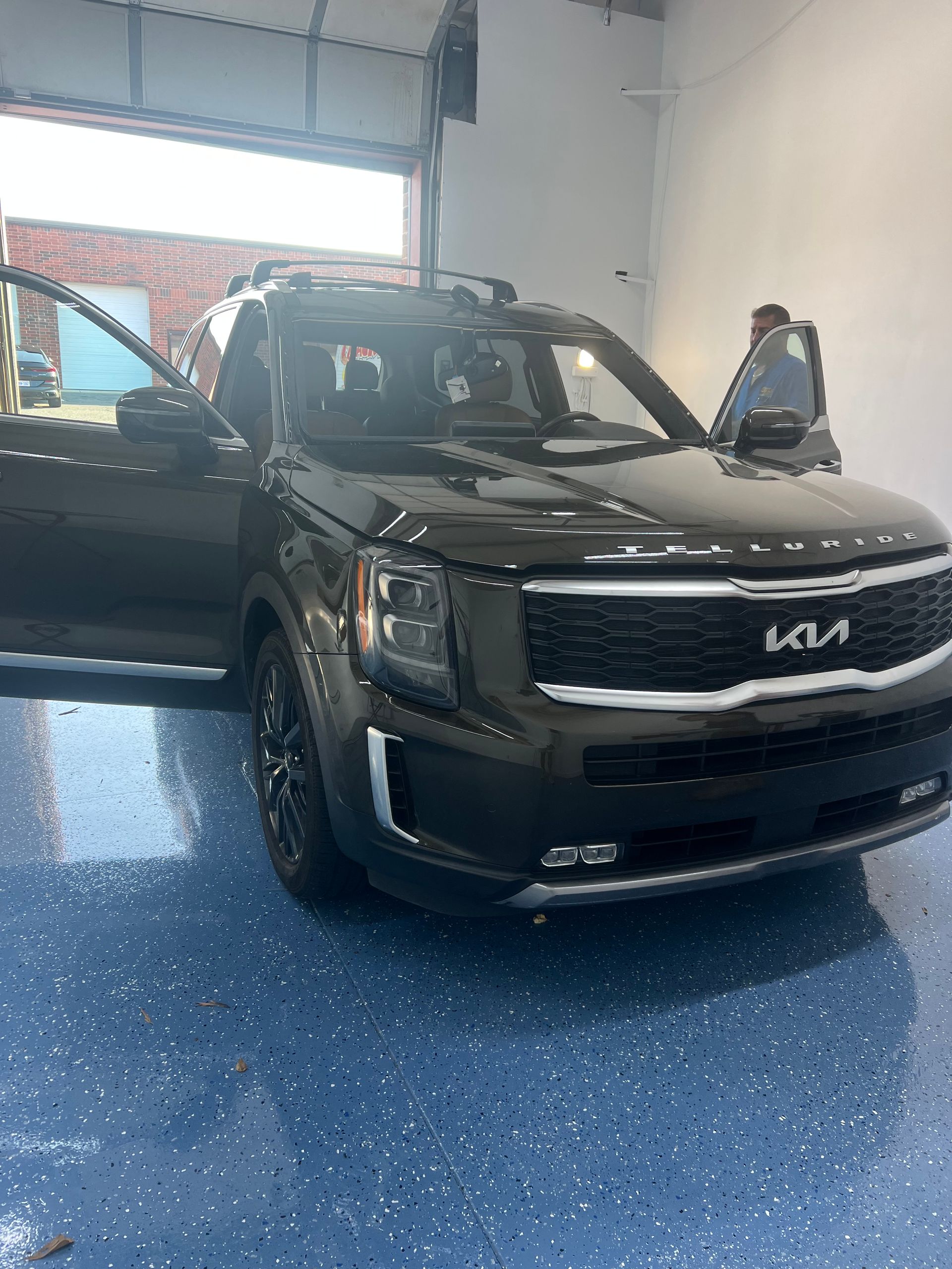 Dark Kia Telluride SUV with doors open, parked in a garage with a person inside.