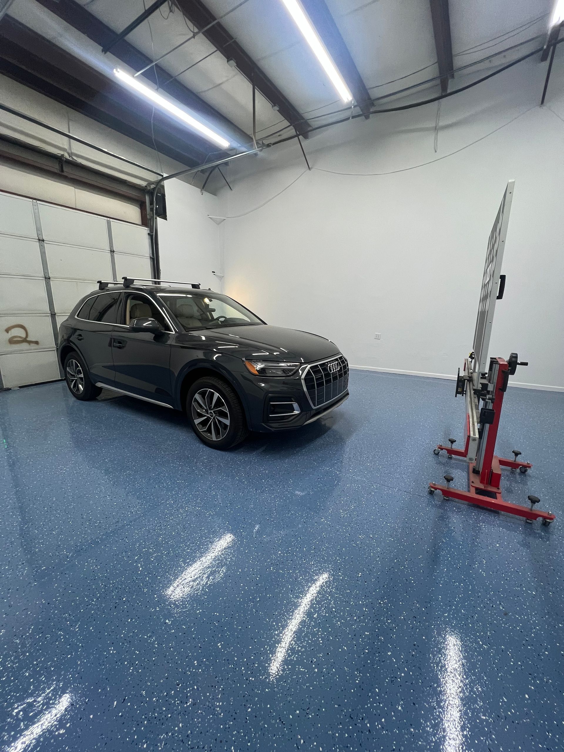 Dark gray SUV inside a garage with alignment equipment. Blue epoxy floor.