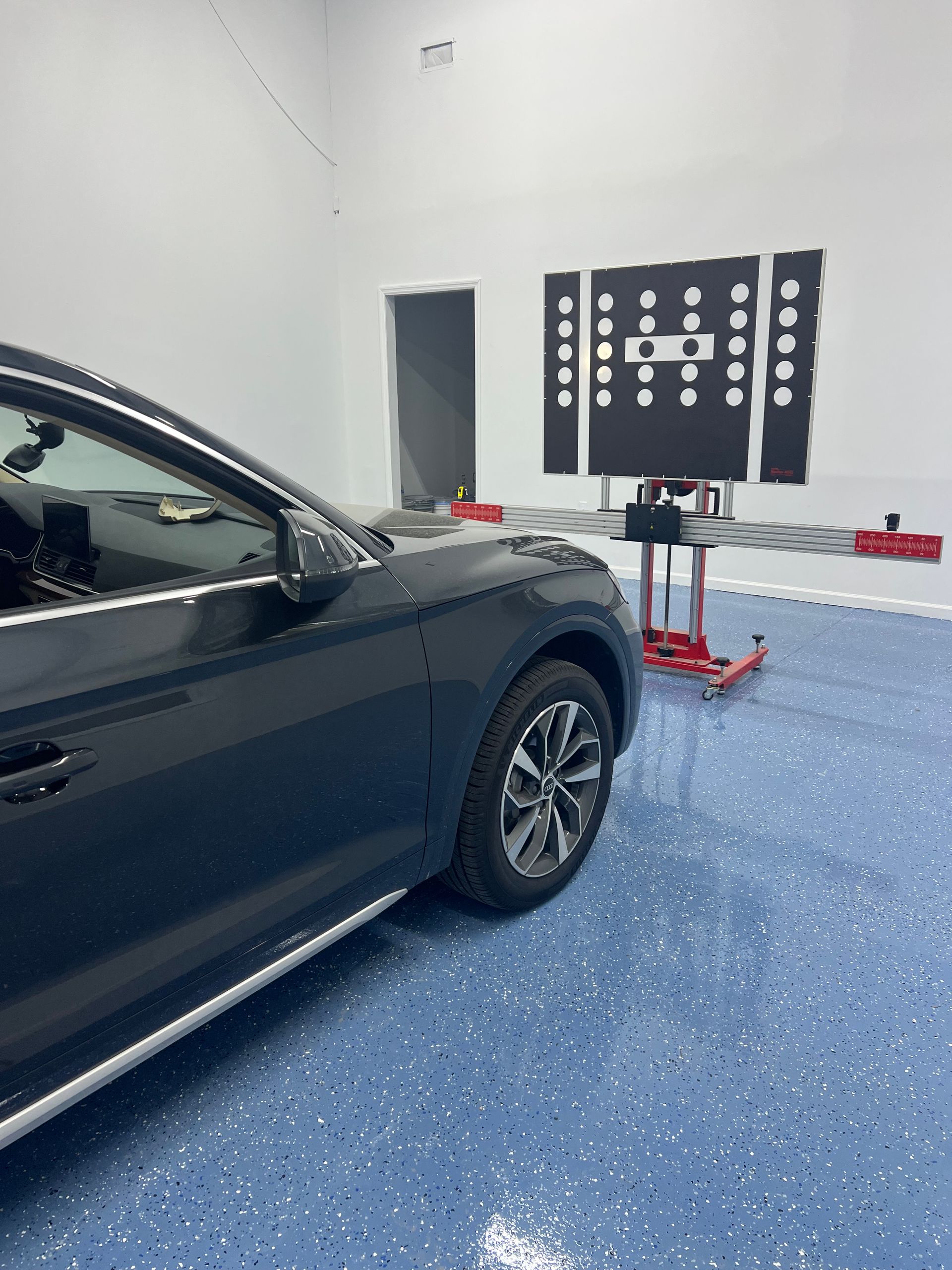 Dark-colored SUV in a garage undergoing wheel alignment. Alignment machine and targets are visible.