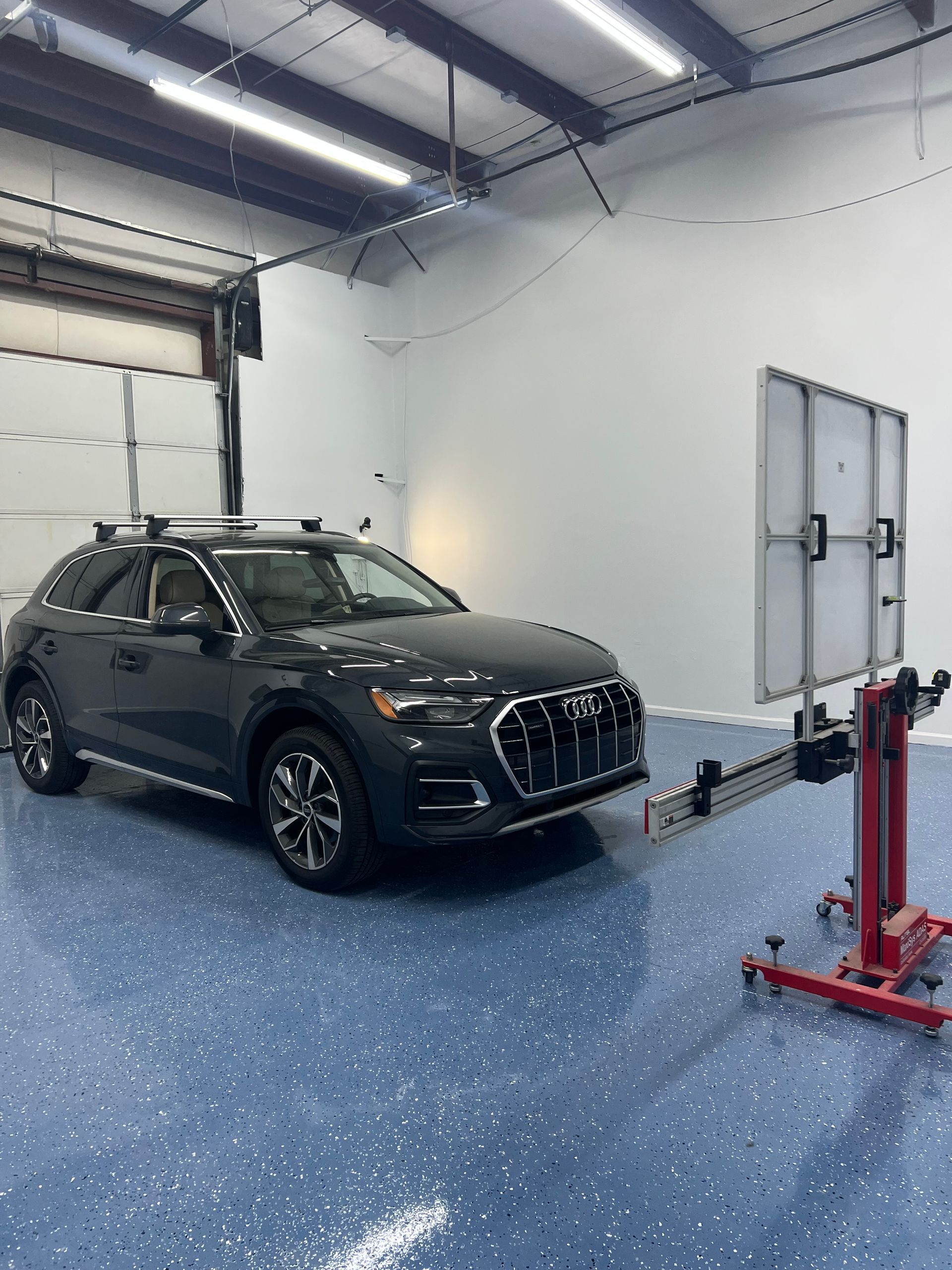 Dark gray Audi SUV in a shop, being inspected with alignment equipment. Blue speckled floor.