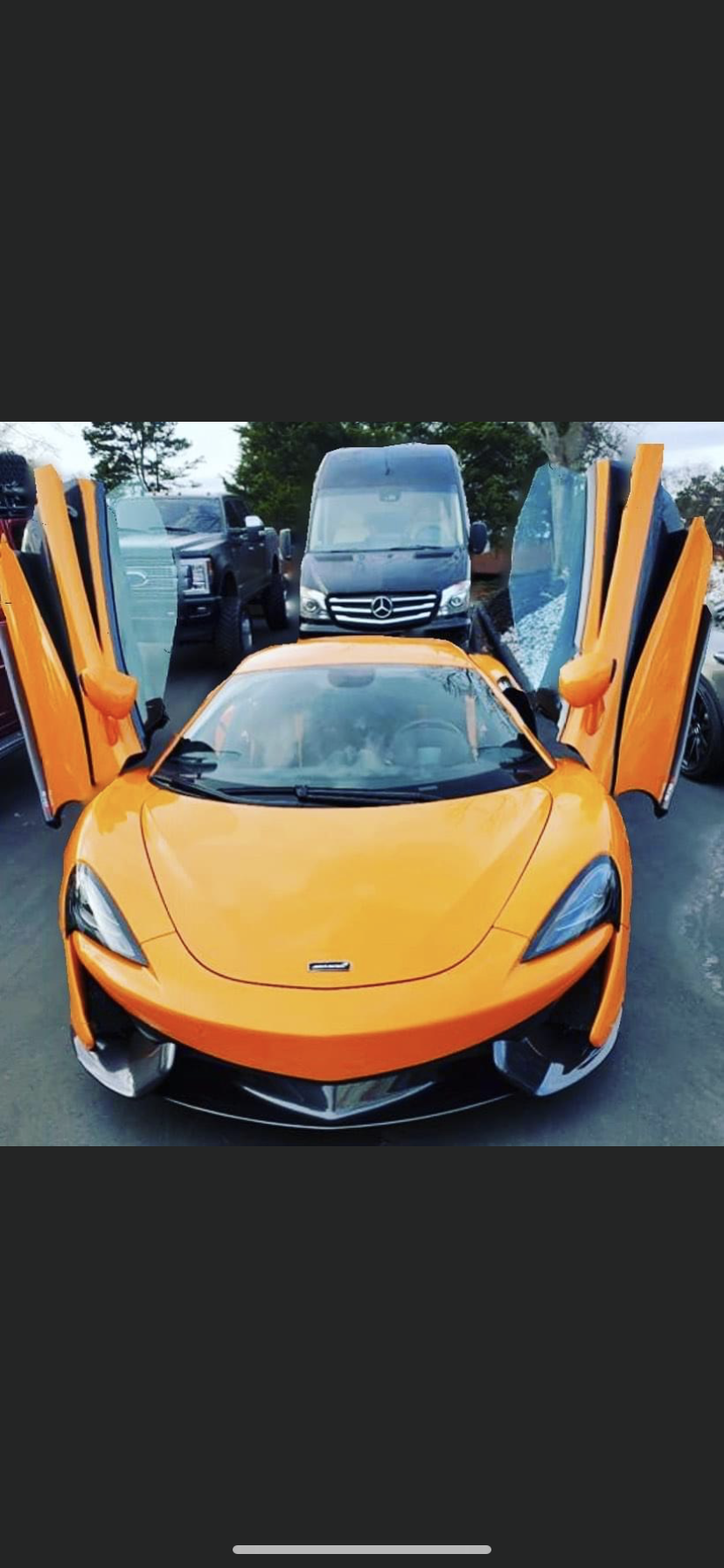 Bright orange McLaren with doors open, parked outdoors.