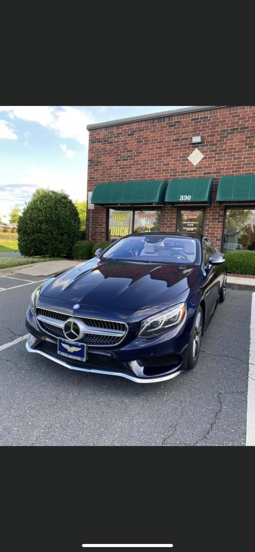 Dark blue Mercedes convertible parked in a parking lot, near a brick building with green awnings.